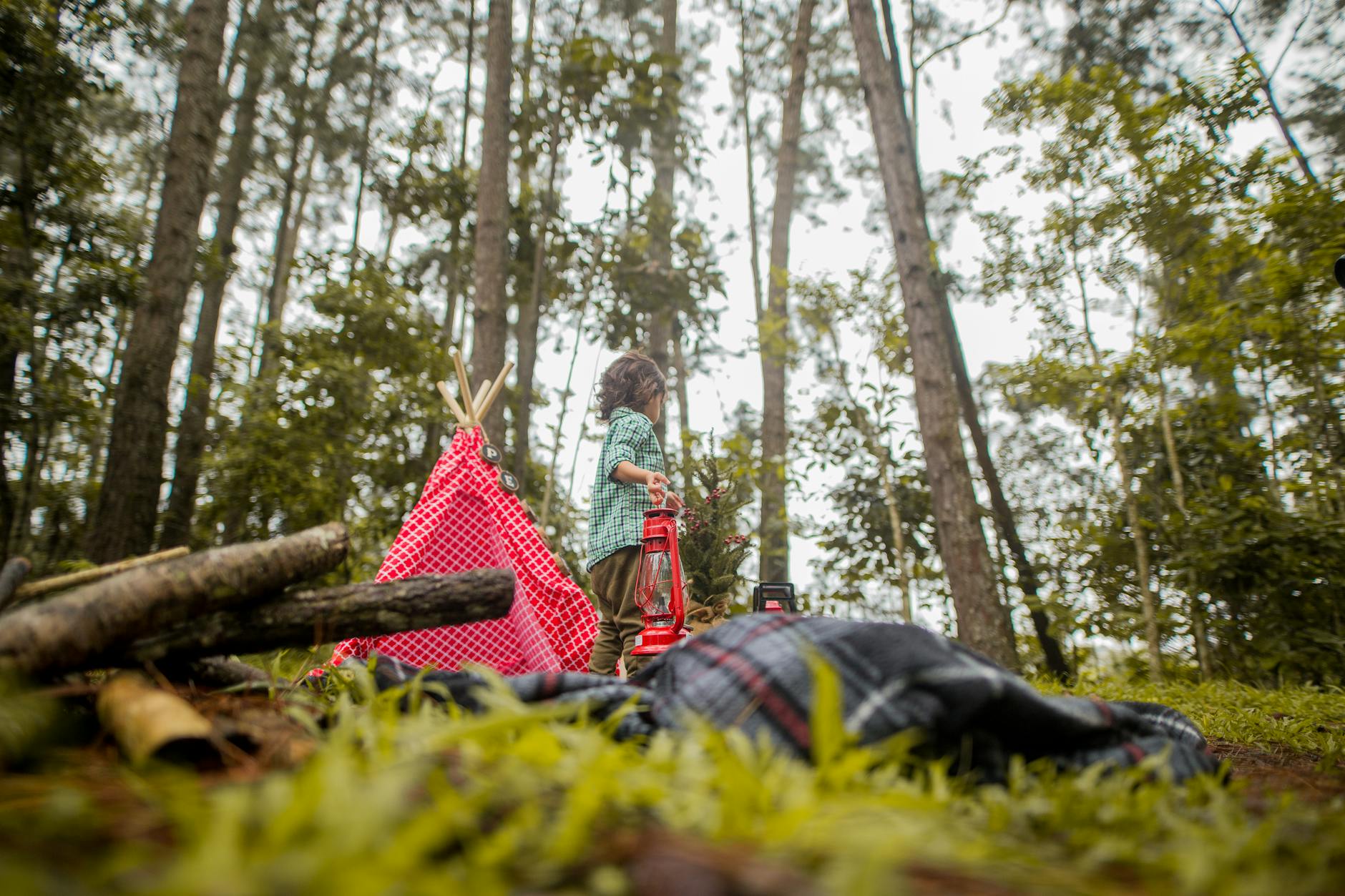 A photograph of boy with a lantern on hand on a campsite.