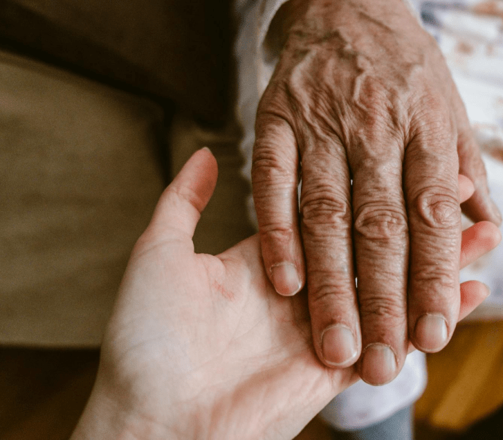 A close up photograph of two hands. An old hand on a young hand. 