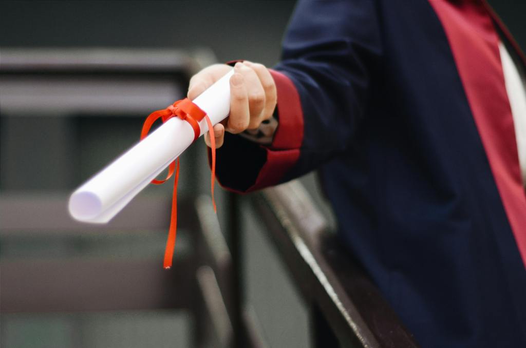 A photograph of a hand holding a rolled paper with red ribbon. 
