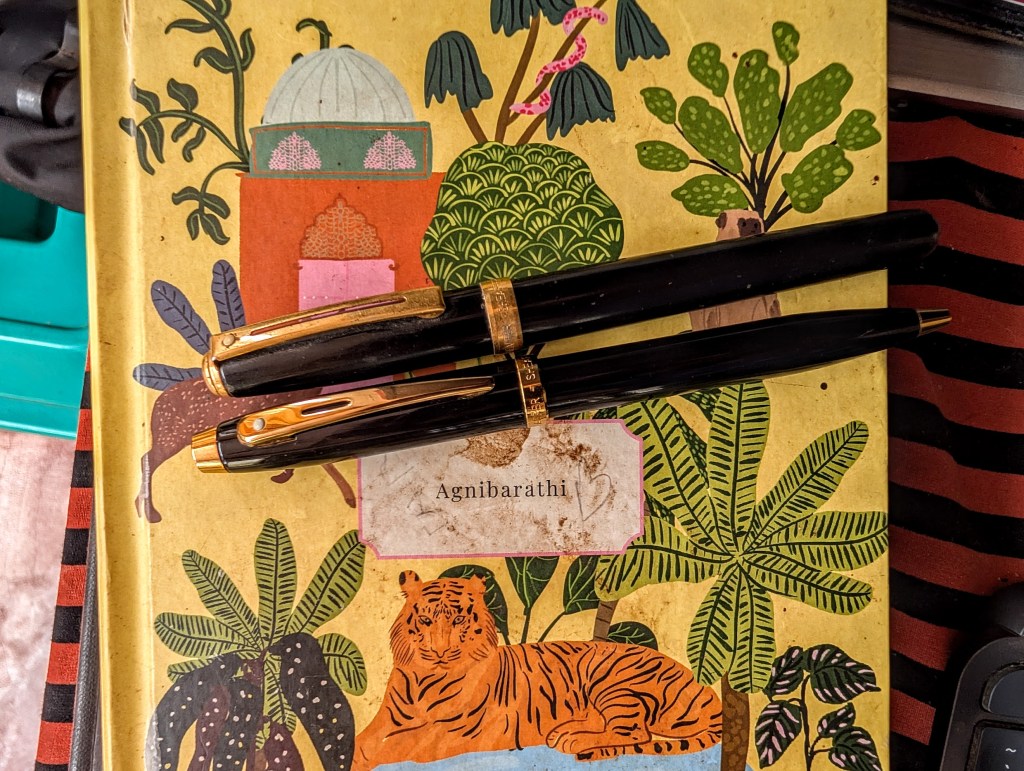 A photograph of a notebook and two pens. 